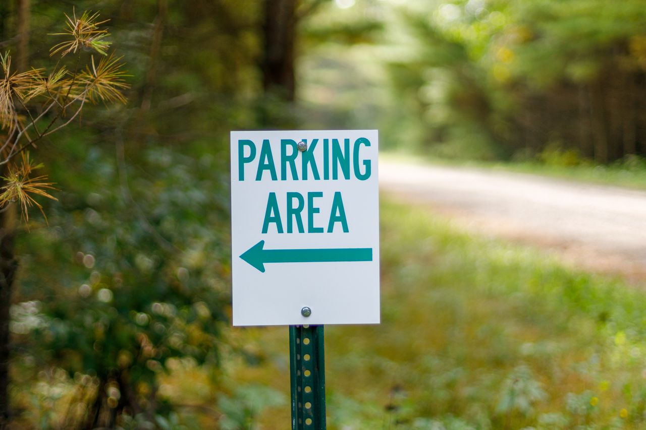 Close-up of a parking area sign with green text on a forest pathway.